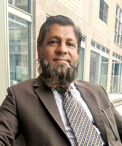 マムンさんのポートレイト　茶色のスーツにネクタイをした、立派な顎髭の男性