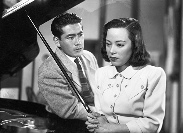 映画『醜聞（スキャンダル）』のワンシーン。傘を持ってうつむいている女優と、見つめる男優。