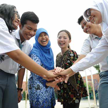 民族衣装などをまとった人物数人が円陣を組んで中央で手を重ねている