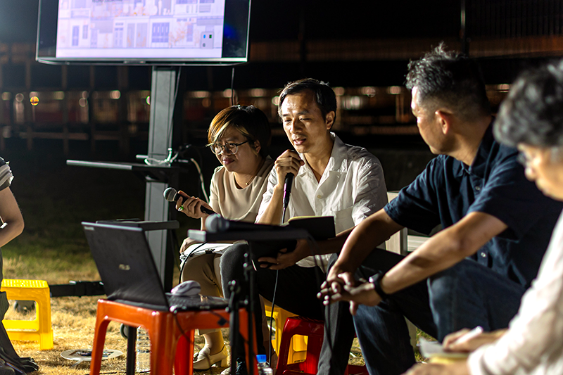 プラスチックの椅子に座りマイクを手に静かに話す男性