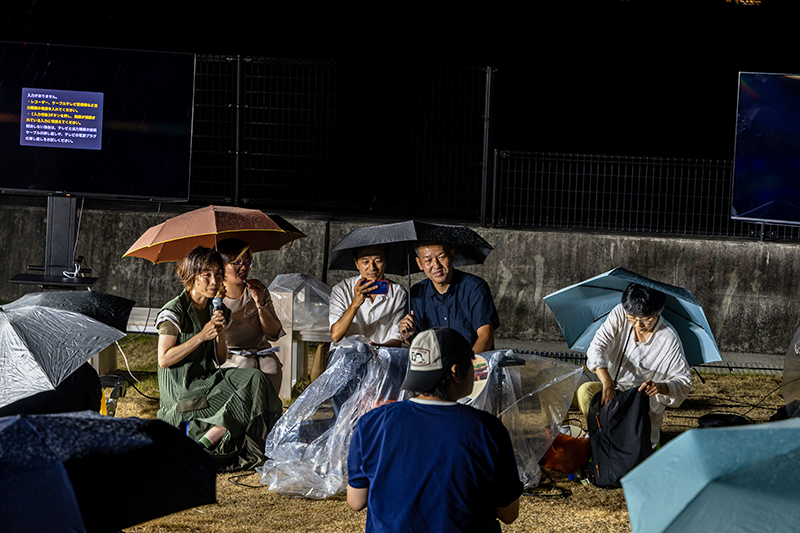 傘の下に寄り添いながら話をする登壇者たち