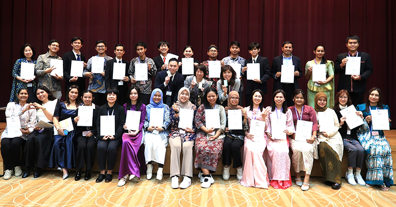 講堂の舞台で終了証を手に2列に並んだ30名ほどの研修参加者の集合写真