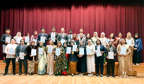 背景に赤いカーテンのかかった舞台の上下に2列に並んでいる。銘々が証書を手に持ち、首からメダルを下げている。